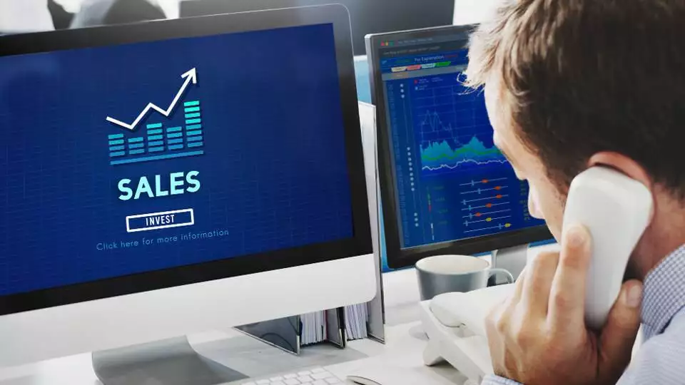 a man talking on the phone while looking at a sales graph on a computer screen, focused on increasing sales right now.