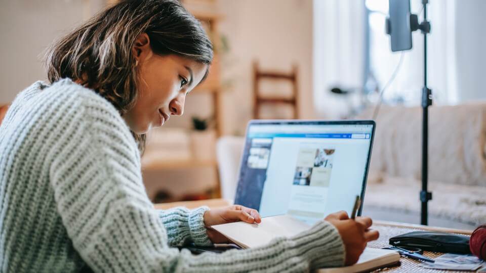 A woman creating cornerstone articles that Google loves while writing in a book.