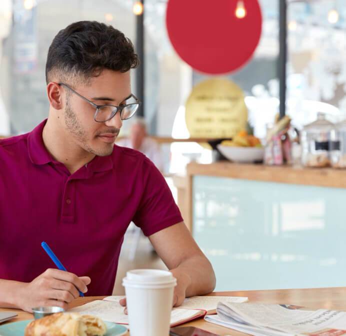 a young man passionately creating cornerstone articles that google loves, while sitting at a table and diligently writing in a notebook.