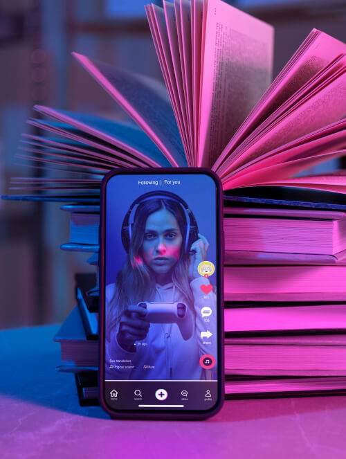 smartphone displaying a social media video of a young woman, surrounded by a stack of open pink books with neon lighting, offering free advice on making money.