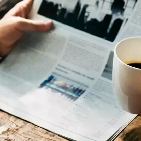 a person newsjacking their way to followers and sales while reading a newspaper with a cup of coffee.